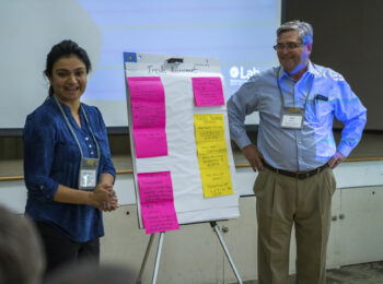 Innovation Charrette Discussion những người sáng tạo đang thảo luận về ý tưởng được đề xuất bên cạnh một cuốn sổ tay lớn có dán ghi chú trên đó